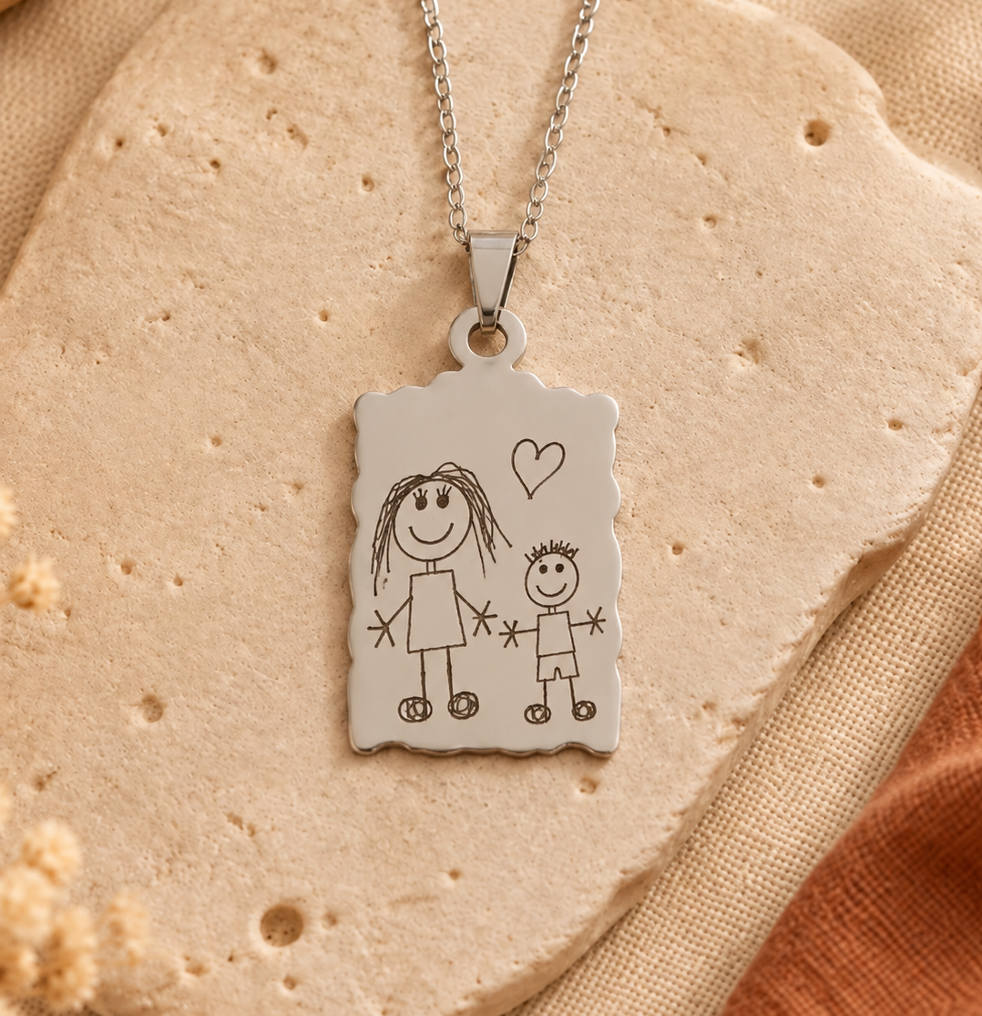 Collier argenté avec pendentif rectangulaire gravé d’un dessin d’enfant représentant deux personnages et un cœur