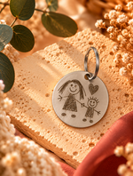 Porte-clé rond personnalisé en acier inoxydable avec gravure d'un dessin d'enfant représentant une maman et son enfant, accompagné d'un cœur. Cadeau souvenir unique – Dénésis.